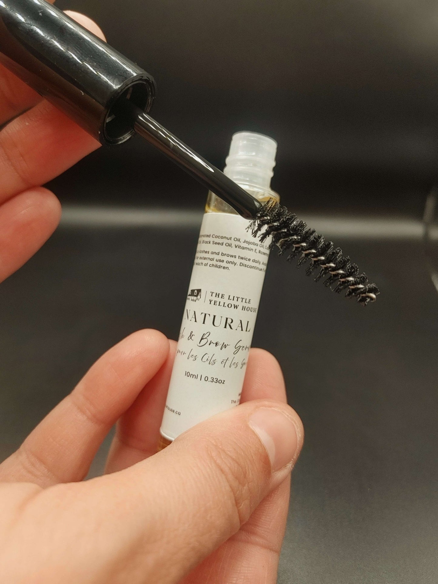 Hand holding a small bottle with a brush and mascara wand for the lash and brow serum 