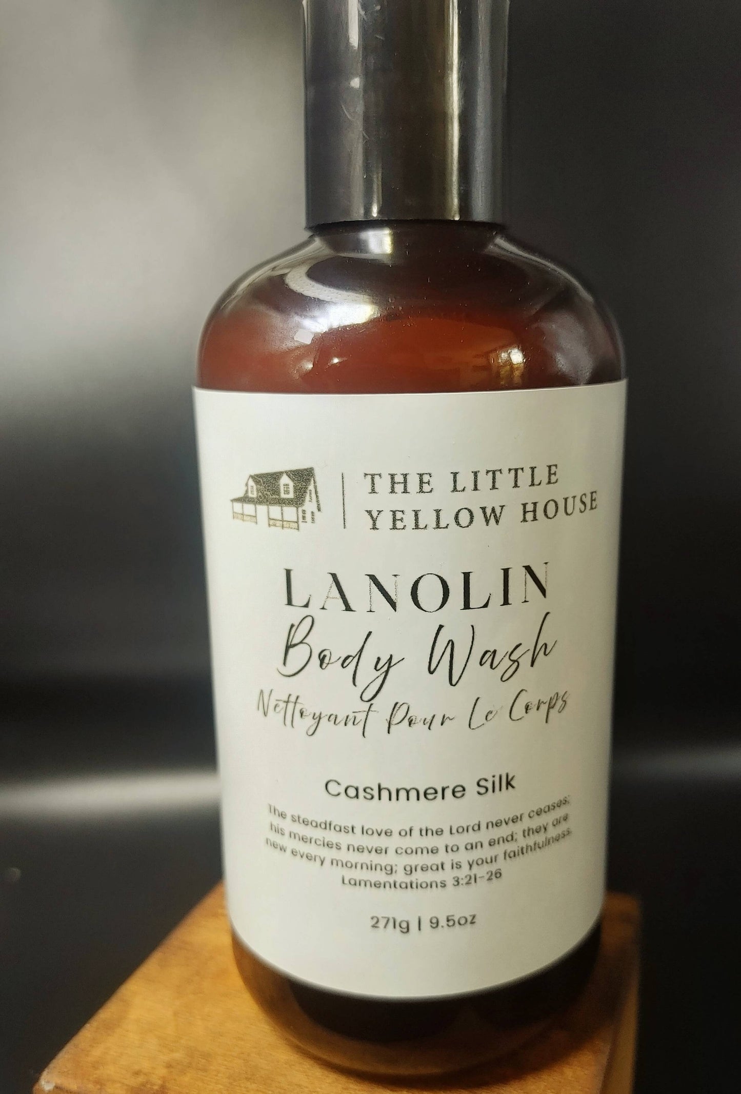 Bottle of Cashmere Silk Lanolin Body Wash from The Little Yellow House on a wooden block with a blurred background.